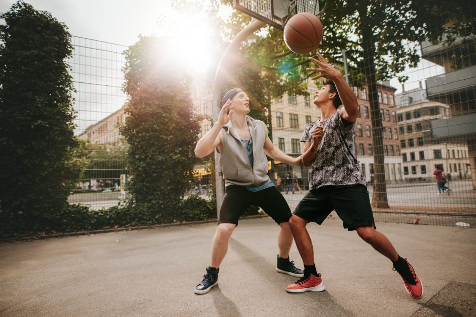 Teenage friends playing basketball against each other on an outdoor court. Two young men playing a game of basketball.