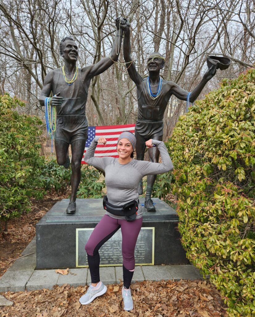 Leslie Pascual-Esposito poses with her arms up after a recent run in in front of the Johnny Kelley marathon statue in Newton, Massachuestts.