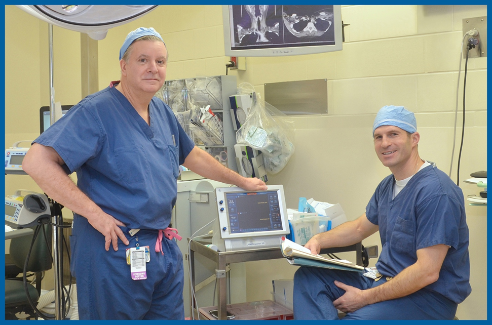 Drs. Gregory Randolph (left) and Jeremy Richmon in the OR wearing scrubs, posing with their surgical equipment.