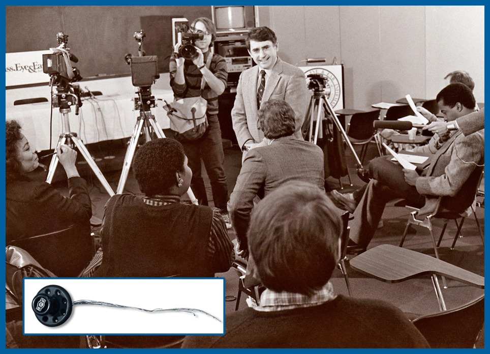 Dr. Joseph B. Nadol center/facing camera is speaking with a room full of reporters at a press conference in 1984 after her performed he first cochlear implant in New England (inset photo of cochlear implant).