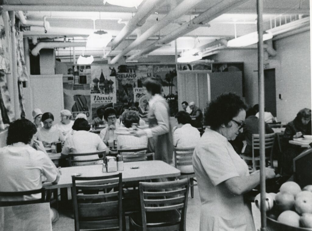 Black and white photo of people sitting and eating in the Mass Eye and Ear cafeteria in 1972 before a renovation and move to the seventh floor of the hospital.