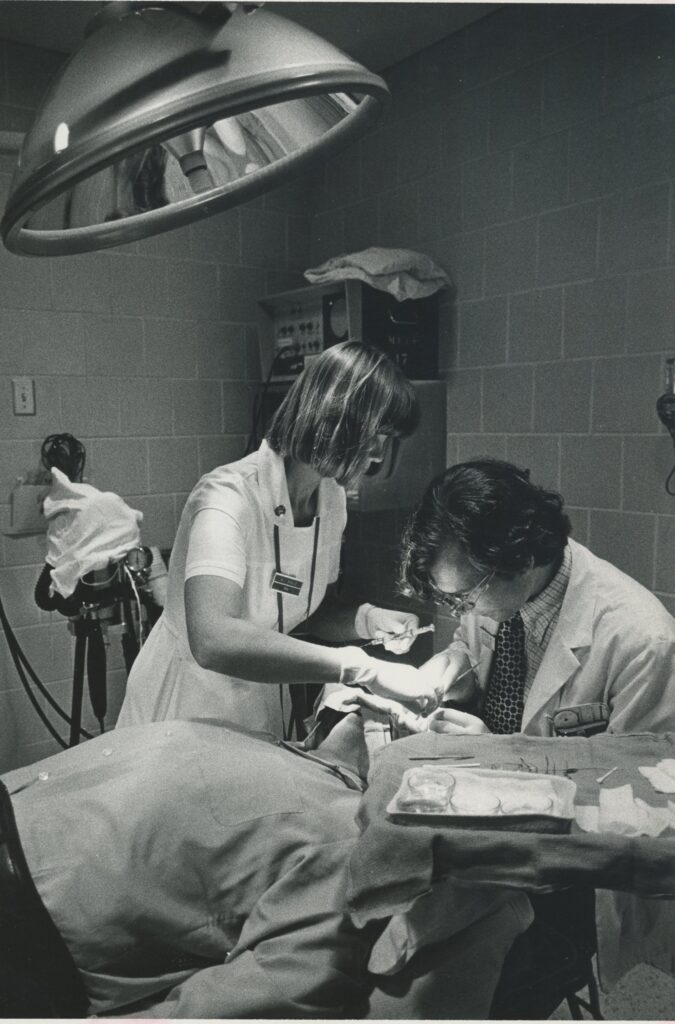 Marcia Palo, RN, assisting Thomas Hedges, MD, in surgery, 1970s