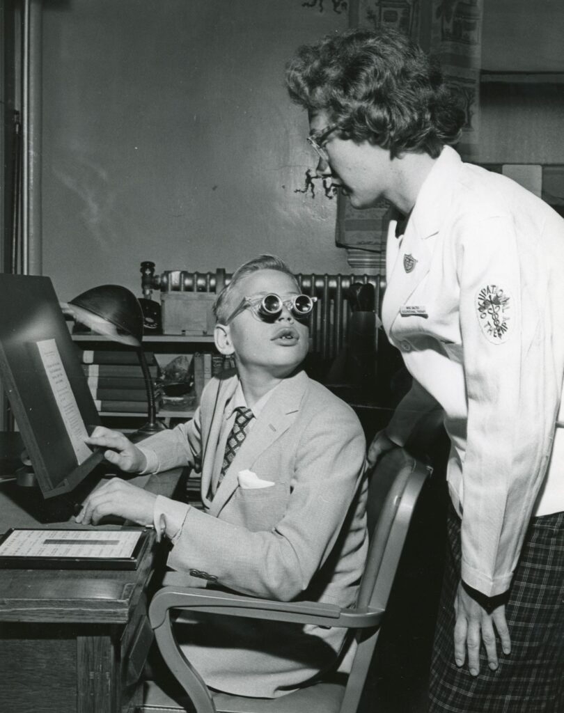 A boy uses telescopic lenses to read in the Low Vision Clinic, 1956.