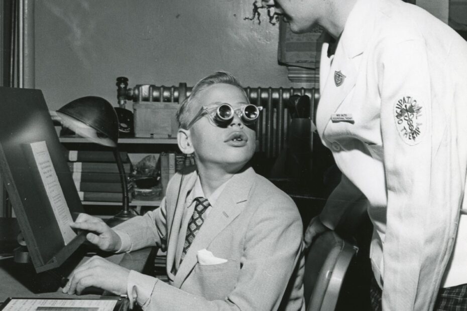 A boy uses telescopic lenses to read in the Low Vision Clinic, 1956.